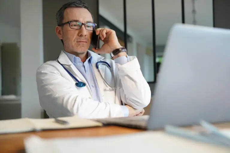 Doctor in office working on laptop talking on phone